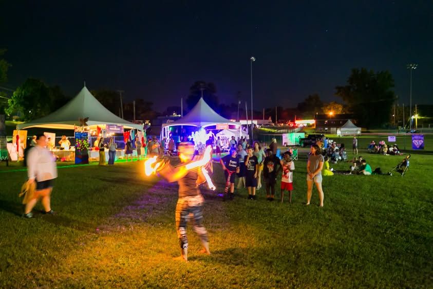 PaoliFest at night with a fire performer, tents, and festivalgoers